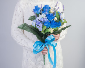 Women  in knit sweater with a bouquet of lilies of the valley blue  flowers in her hands. selective focus on white background.