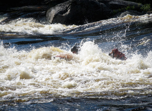 Men on an inflatable catamaran overcome the threshold of the turbulent river. Catamaran is not visible. 