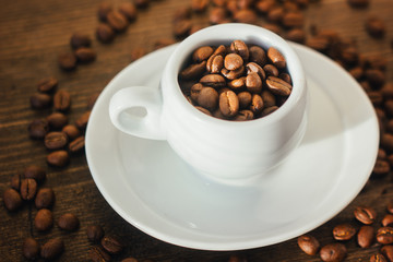 Coffee beans on white coffee cup over the wooden table.