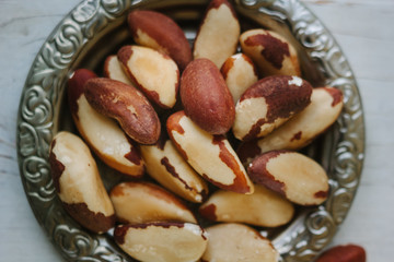 Brazil nuts in metal plate over the white wooden table.