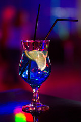 Beautiful glass with a cocktail at the bar on the table. Night club. Alcoholic drink blue color with a lemon on the inside