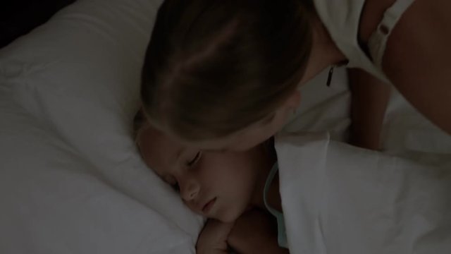Caring mother kissing her little daughter at bedtime