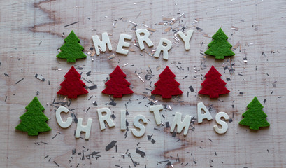 Wooden white "Merry christmas" with christmas trees and sparkly decor on wooden background.