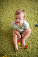 Little girl in plays on the green fluffy carpet