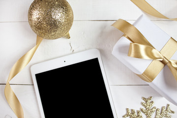Digital tablet with golden christmas decoration on white wood background