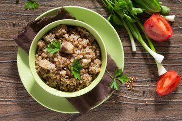 Buckwheat with meat stew and fresh vegetables on a wooden table.