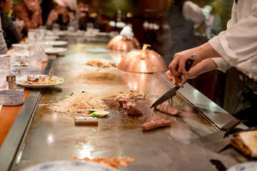 Hand of professional chef cooking beef steak on hot pan, in front of Customer