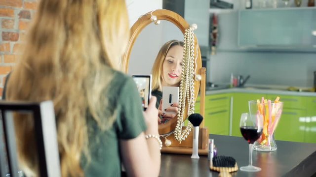 Happy girl looking at the mirror and doing photos on smartphone
