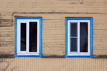 Two windows in the blue framed in a wooden house, painted beige paint
