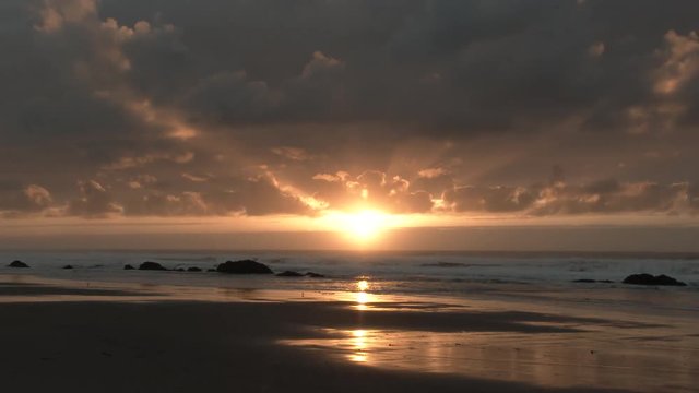 Colorful clouds light up the sky as sun sets over the Pacific Ocean at the Oregon Coast, time lapse day to night.