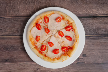 pizza with ham and tomato on wooden table, top point of view