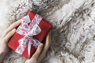 young woman is untying wrapped in red kraft paper gift for happy holiday on fur coat