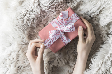 young woman is untying wrapped in red kraft paper gift for happy holiday on fur coat