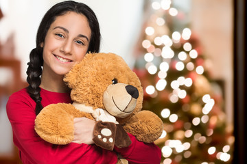 Smiling girl holding a teddy bear. Christmas tree in the background