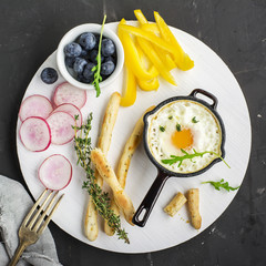 Scrambled eggs for breakfast in the batch cast iron skillet on a white board with chopsticks angered and vegetables