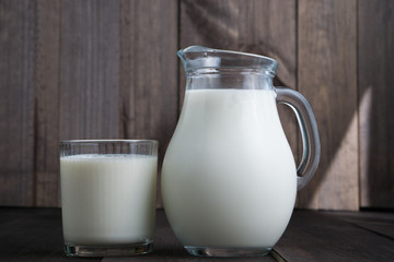 full jug and glass with milk on wooden background