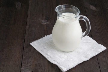 full jug of milk on white tissue napkin and wooden background