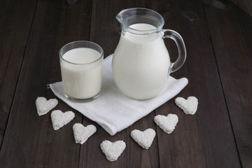 jug and glass with milk and heart cookies on white tissue napkin and wooden background