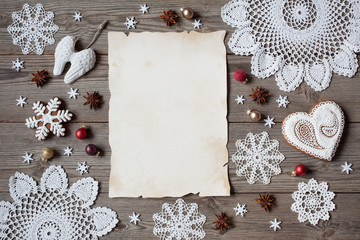 Obraz na płótnie Canvas Christmas wooden background with lace snowflakes, gingerbread and blank greeting list