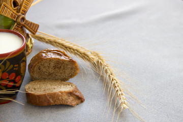 Bread and wheat with a cup of milk on a gray fabric.