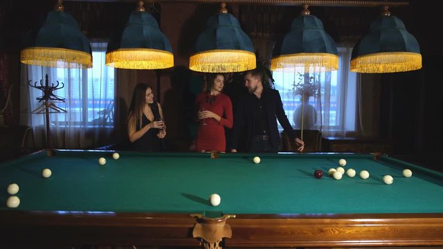 a man plays Billiards and two young beautiful women watching the game