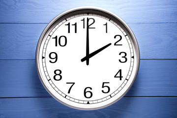 Round clock shows shows at 2 o'clock, clock on blue background