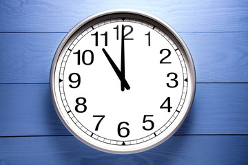 Round clock shows shows at 11 o'clock, clock on blue background