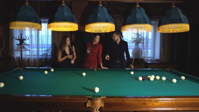 a man plays Billiards and two young beautiful women watching the game