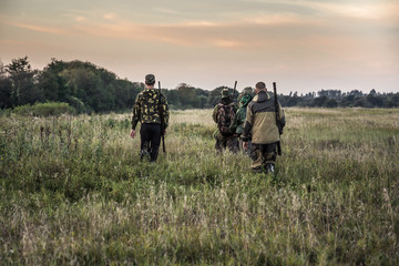 Jagdszene mit Jägern, die während der Jagdsaison an bewölkten Tagen bei Sonnenuntergang mit stimmungsvollem Himmel durch ländliches Feld gehen