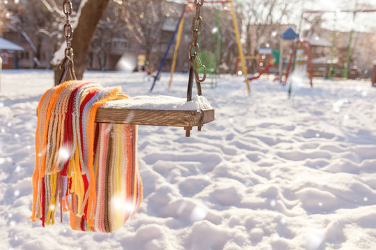Empty swing with snow and checkered scarf on it in the winter sunny day. City park in the snow. Coloring and processing photo.
