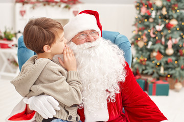 Boy telling wish in Santa Claus's ear against Christmas tree