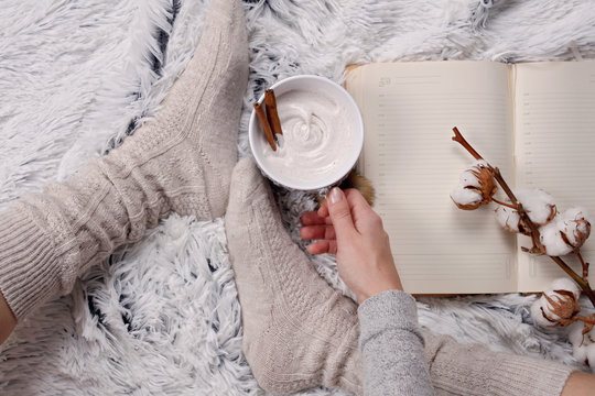 Woman wearing cozy warm wool socks, reading a book, drinking hot drink lose up. Warmth concept. Winter clothes