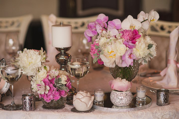 Table setting at wedding reception. Floral compositions and candles on decorated dining table.
