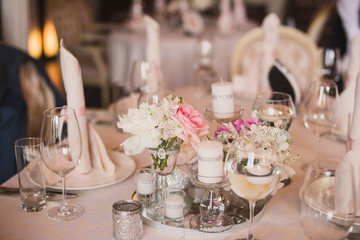 Table setting at wedding reception. Floral compositions and candles on decorated dining table.