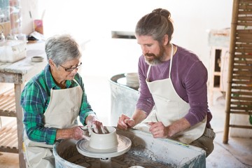Male potter assisting female potter while making pot