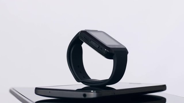 Black smartwatch on top of smartphone and tablet moving around, isolated on grey background, modern gadgets. Close up, seamless loop, 4K Ultra HD.