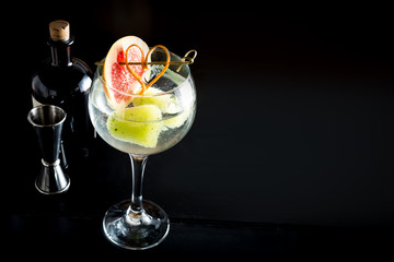 Gin tonic drink cocktail fancy glass black background tonic water ice garnish fresh fruit craft cocktail cucumber orange peel decoration measure bottle lime peeler grapefruit