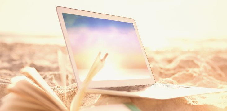 Composite image of open book and laptop on sand