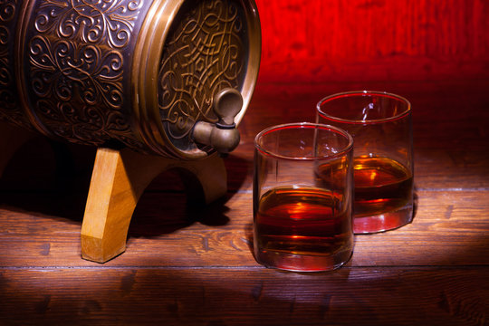 Glasses of whiskey and small barrel on wooden table