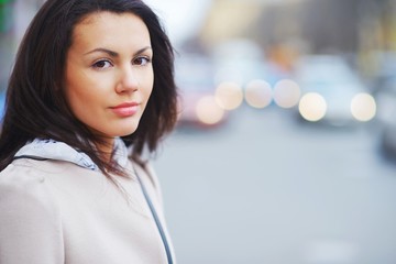 Portrait of a young brown-eyed brunette girl on a beautiful blurred background city street, close-up.