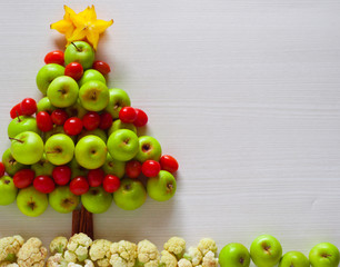 Christmas tree decorations from apple and cherry tomatoes with a white wooden background