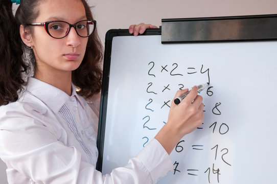 Schoolgirl with glasses shows the multiplication table on the  board