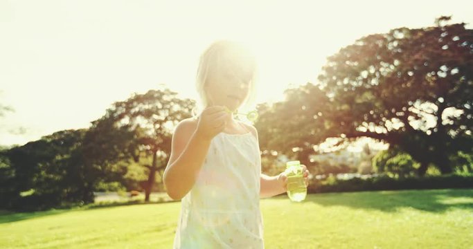 Cute young girl playing outside blowing bubbles in park
