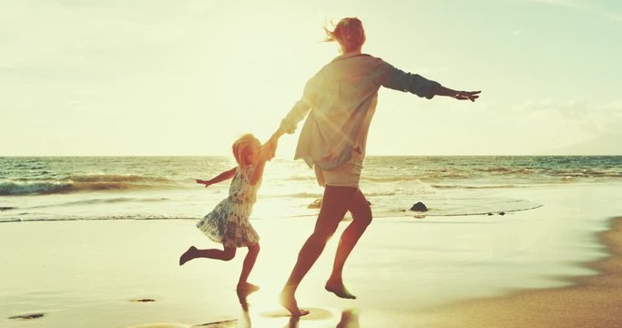 Mother and daughter walking and playing on the beach at sunset