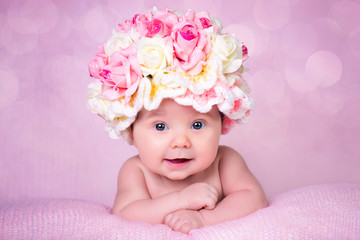 Newborn baby girl in the hat rose smiles. Portrait on a pink background