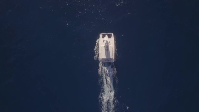 Aerial top view of white yacht sailing in dark blue water of ocean leaving foamy trail. Sea trip