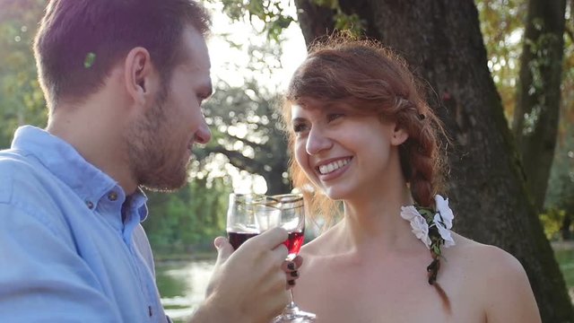 young couple makes a toast in the park and drink red wine