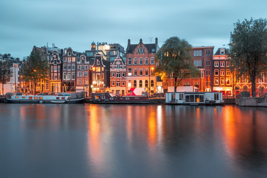 Amsterdam canal Amstel with typical dutch houses and boats during twilight blue hour, Holland, Netherlands.