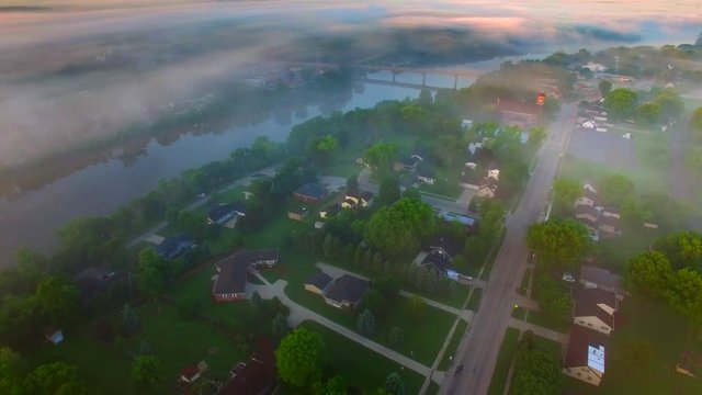 Small town America with river, bridge, under spectacular foggy sunrise, aerial view.
