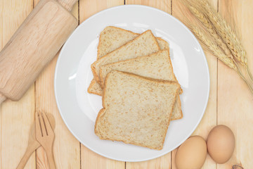 Sliced wholemeal bread on white plate with wheat ears and egg on wooden table background, Top view